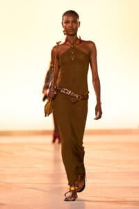 Model walking the runway in a brown halter-knit dress with a leather belt and small bag.