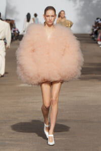 Model walking the runway in a oversized pale pink fluffy dress, white Mary Jane heels, slicked-back hair.