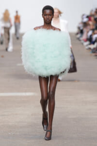 Model walking a runway in a oversized mint-green fluffy off-shoulder garment.