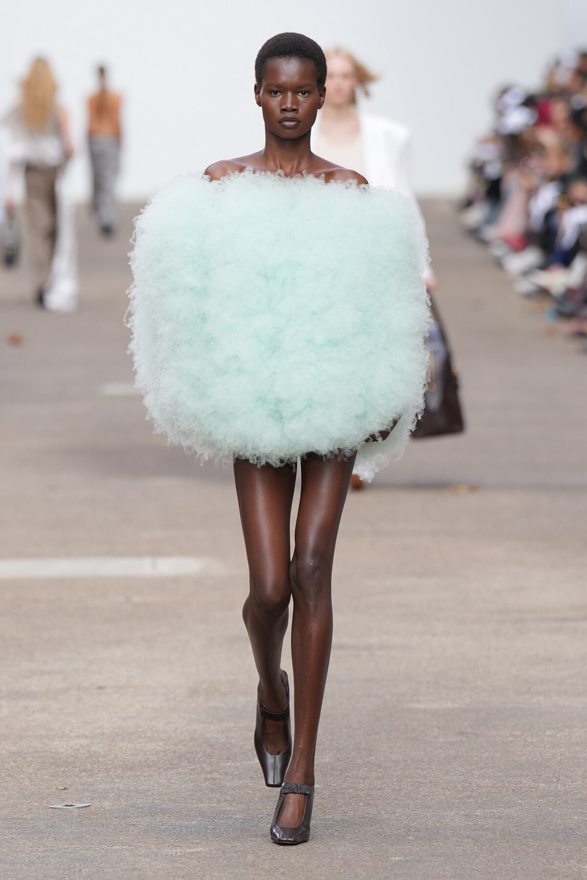 Model walking a runway in a oversized mint-green fluffy off-shoulder garment.
