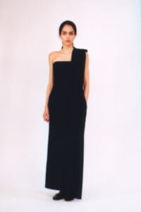 Model wearing a floor-length black one-shoulder gown, standing against a plain light background.
