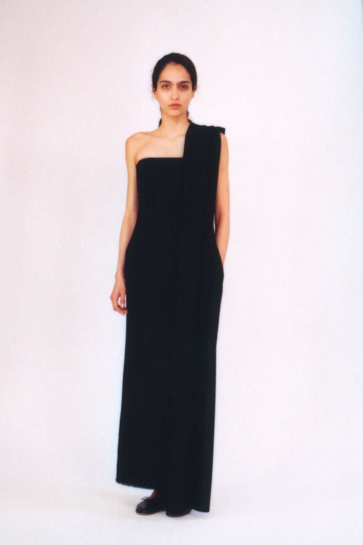 Model wearing a floor-length black one-shoulder gown, standing against a plain light background.