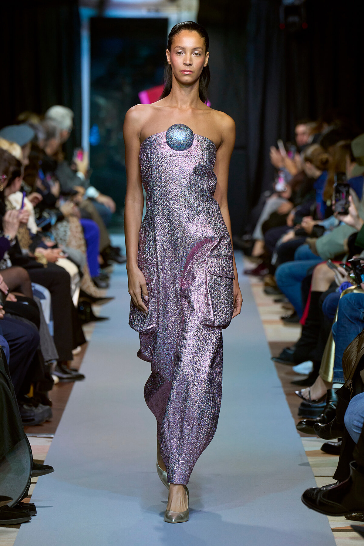 Model walks the runway in a metallic lavender strapless gown with a round blue gem at the bust.