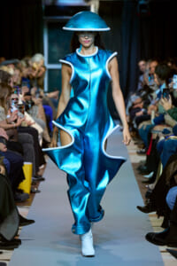 Model walks a futuristic blue metallic dress with white trim and matching dome hat on runway.