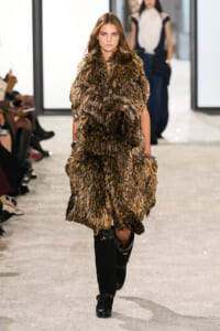 Model walking runway in a voluminous brown shaggy fur coat over black knee-high boots.