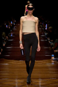 Model walks the runway in a beige bandeau top, black high-waisted leggings, and a futuristic black visor eyewear.