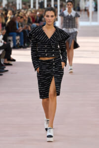 Model walks the runway in a black-and-white striped cropped blazer and matching pencil skirt with front slit and white platform shoes.