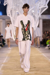 Male model walks the runway in an all-white ensemble with a large camo crocodile print on the shirt.