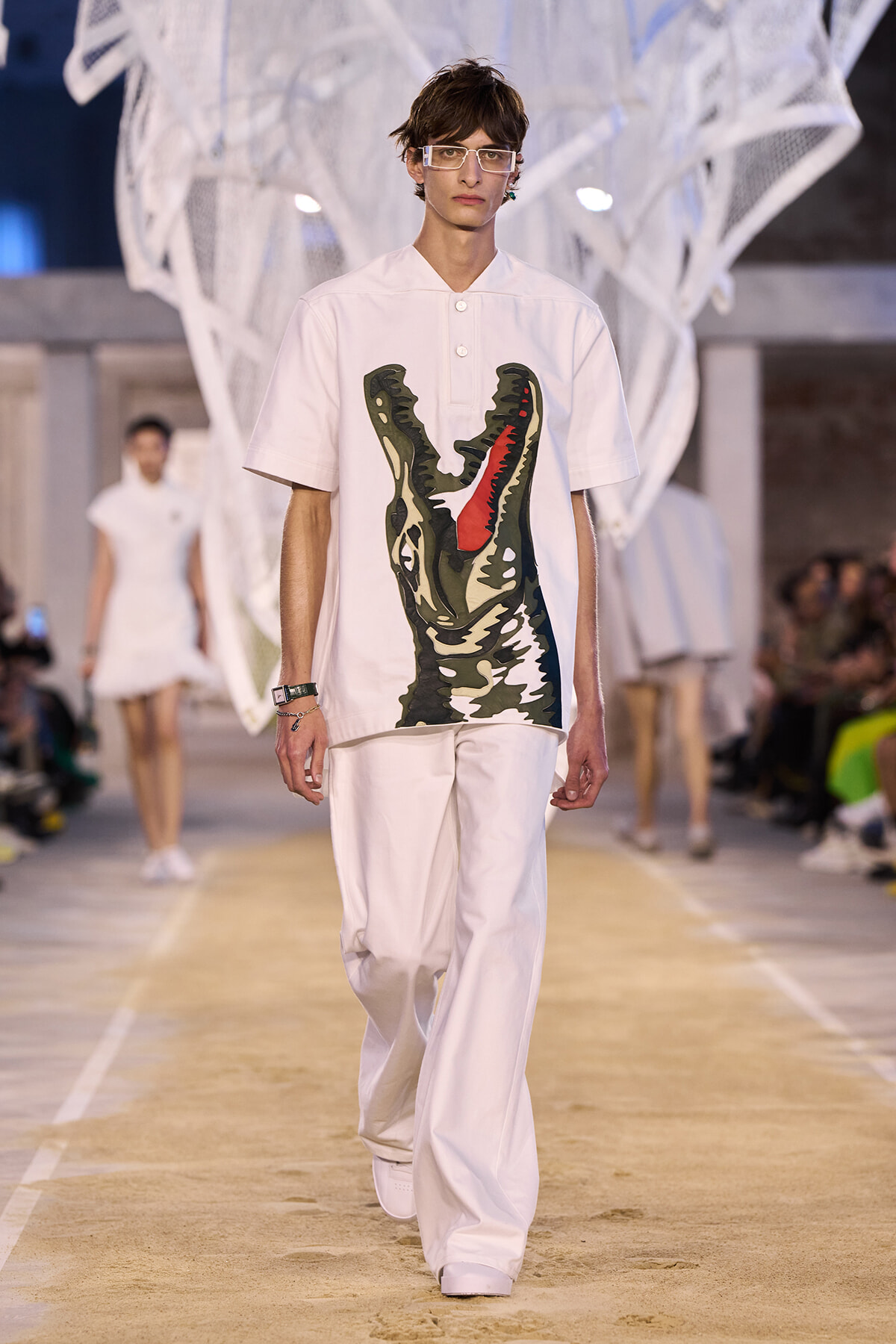 Male model walks the runway in an all-white ensemble with a large camo crocodile print on the shirt.