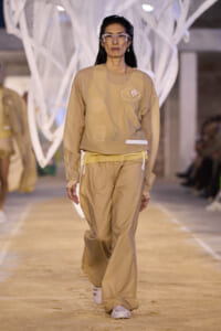 Model walks the runway in a beige cropped top and wide-leg pants, wearing oversized square sunglasses and white sneakers.