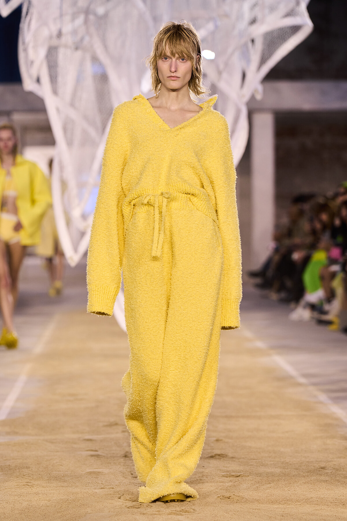 Model walking a runway in a fuzzy yellow knit loungewear set with a V-neck sweater and drawstring pants.