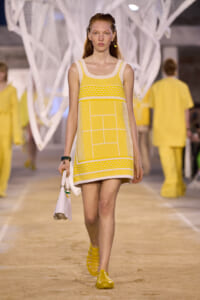 Model walking the runway in a yellow-and-white crochet-inspired mini dress, matching yellow shoes, and a white handbag.