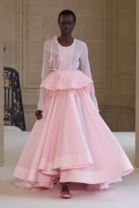 Model in a pale pink ball gown with a layered tutu skirt and ribbon straps walking the runway.