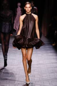 Model walks the runway in a glossy chocolate-brown satin halter dress with a sculpted, bubble-like skirt.