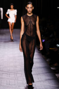 Runway model walks the catwalk in a sheer black dress on a fashion show.”