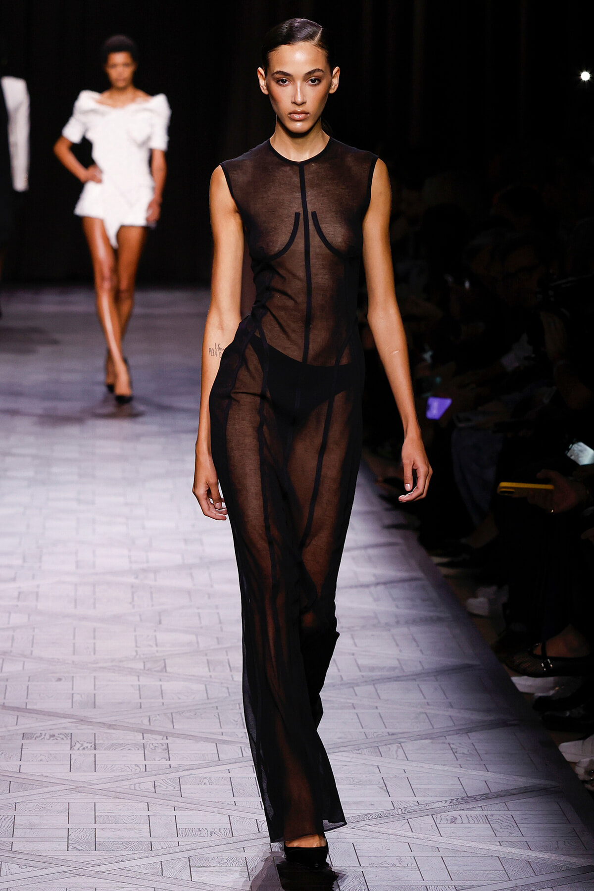 Runway model walks the catwalk in a sheer black dress on a fashion show.”