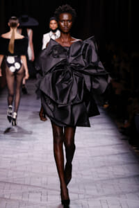 Model walks the runway in a dramatic black avant-garde dress with oversized layered ruffles and sculptural silhouette.