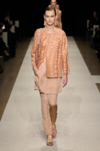 Model on a runway wearing a peach sequin-woven top over matching wide-leg pants, with a beaded shoulder bag and pink sandals.