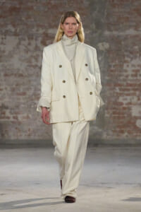 Model walking a runway in a cream double-breasted suit with wide-leg trousers.