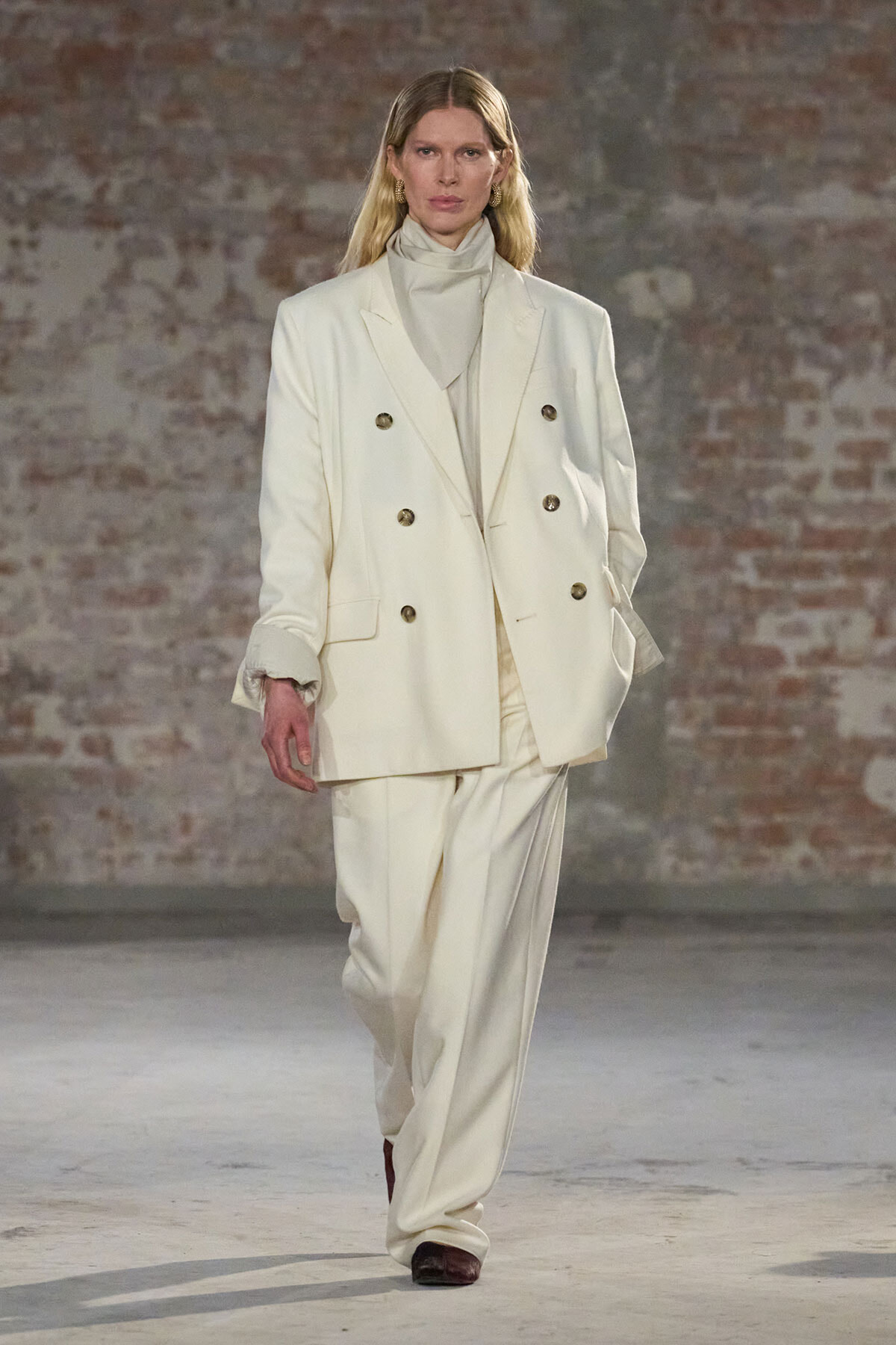 Model walking a runway in a cream double-breasted suit with wide-leg trousers.