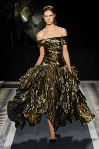 Model wearing an off-the-shoulder gold and black metallic ballgown walking the runway.