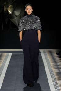 Runway model in a metallic, textured silver top over a navy wide-leg jumpsuit with pockets