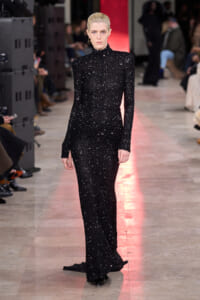 Model walking a runway in a full-length black sequin turtleneck gown with long sleeves and sleek hair.