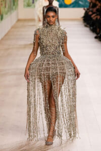 Runway model wearing a metallic fringe gown with a high neck and long dangling strands, walking the catwalk.