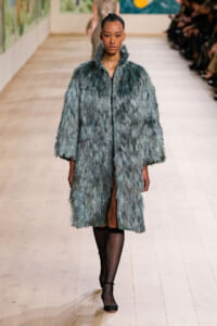 Model walks the runway in a long, teal-blue shaggy fur coat and black fishnet stockings.