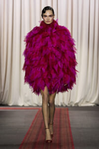 Model on runway wearing a vivid magenta feathered cape dress with a high neck.