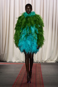 Model walks the runway wearing a voluminous dress made of layered green and turquoise leaves from a leaf-inspired design on the catwalk.