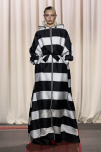 Runway model wearing a black-and-white striped, floor-length dress with a braided rope trim and a waist bow.