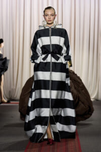 Runway model in a black-and-white striped maxi dress with a waist bow and braided front cord.