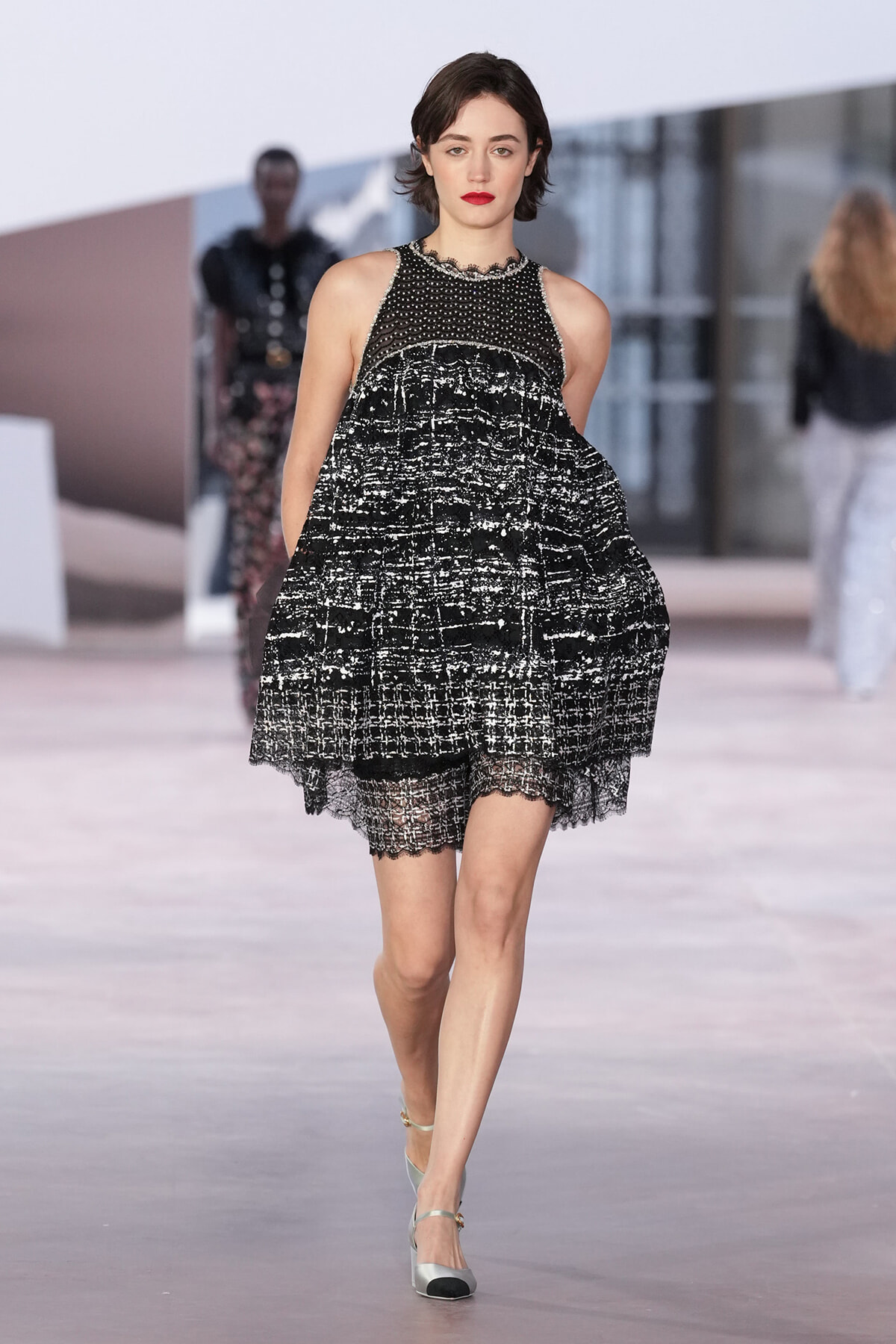 Runway model wearing a black-and-white textured dress with lace hem and red lipstick on a fashion show catwalk.