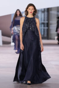 Model on a runway wearing a dark navy sequin sleeveless top over a long flowing navy skirt/gown.