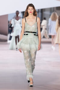 Model on a runway wearing a mint-green sequined top and matching sheer pants with a layered tulle peplum, black belt.