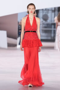 Model walks the runway in a red halter-neck sequin dress with a black belt and a layered ruffle peplum over a flowing chiffon skirt.