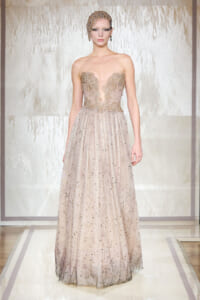 Model on runway wearing a strapless champagne gown with a beaded lace bodice and glittery tulle skirt, headpiece included as part of the look