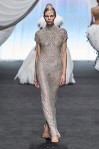 Model walks the runway in a full-length, metallic jewelled mesh dress that is sheer and form-fitting, paired with nude sandals.