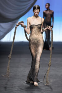 Model walks the runway in a strapless, glittering gold-to-black gown with long rope tassels in each hand.