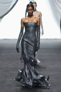 Model walks the runway in a strapless, crocodile-textured charcoal gown with long matching gloves and a dramatic flared train.