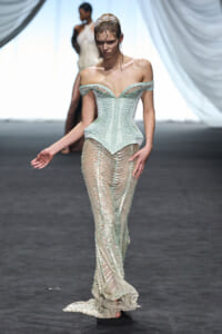 Model on a runway wearing a pale mint off-shoulder corset with a beaded sheer skirt and train.