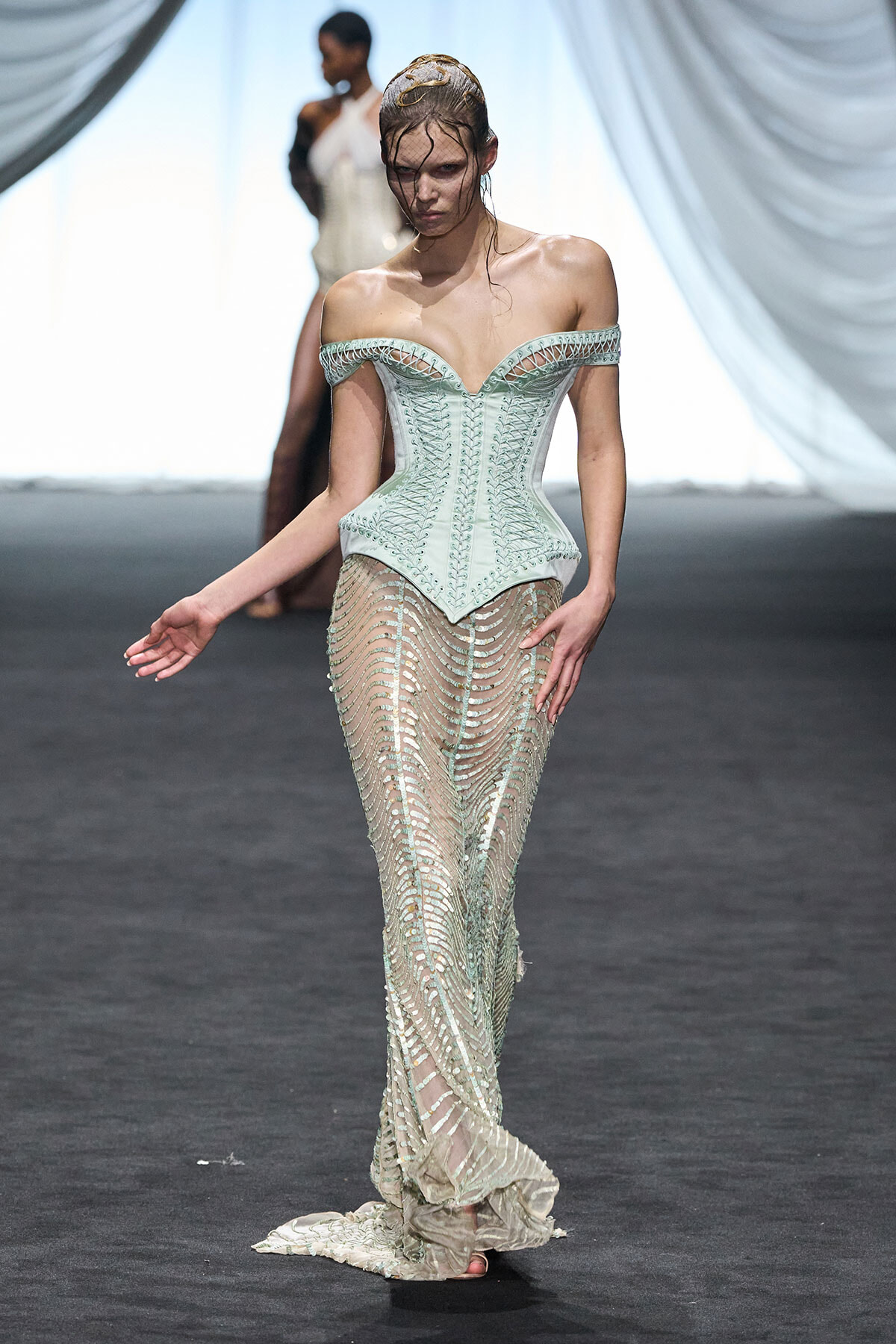 Model on a runway wearing a pale mint off-shoulder corset with a beaded sheer skirt and train.