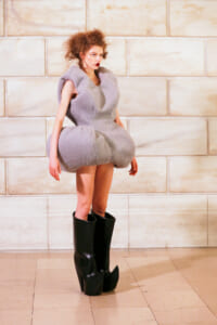 Model on a runway wearing a voluminous light gray plush dress and tall black platform boots.