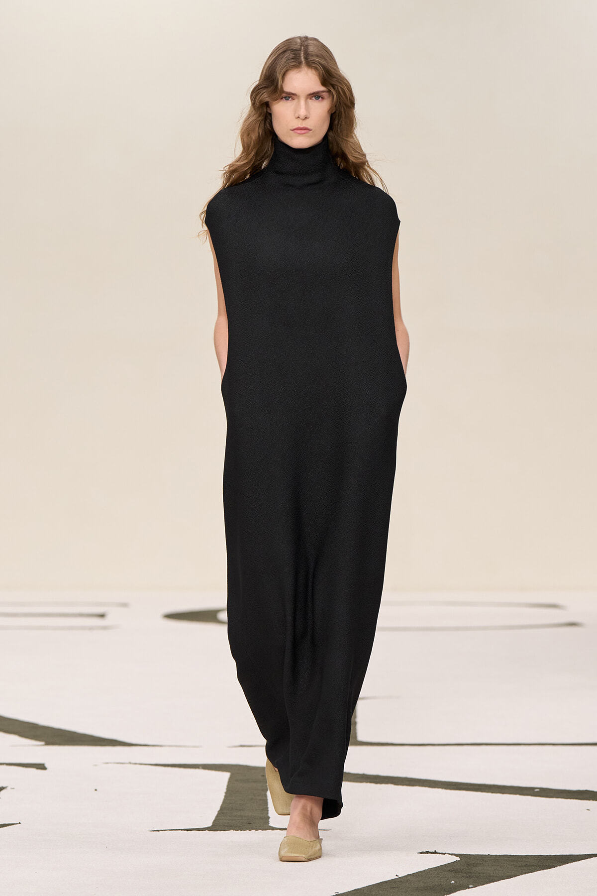 Model walking the runway in a sleeveless black turtleneck jumpsuit with wide legs.
