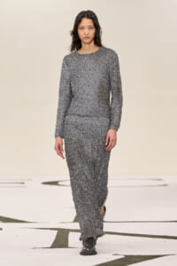 Model walking the runway in a textured gray, long-sleeve knit maxi dress with black shoes.