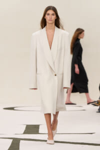 Model walks the runway in a cream oversized blazer dress with a plunging neckline and a single button fastening.