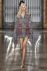 Model walking runway in a multicolored sequin fringe blazer dress with light blue lapels and nude heels.