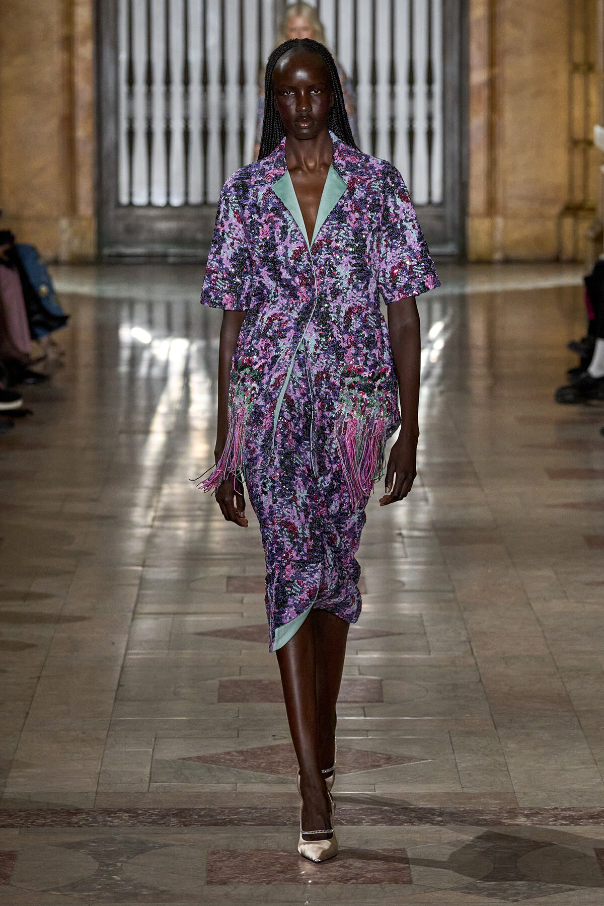 Model walks the runway in a purple floral knee-length dress with mint-green lapels and pink fringe detailing at the hem.