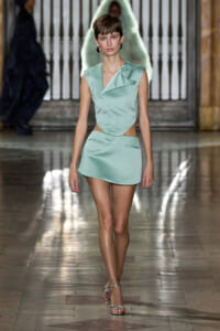 Model walks down runway in a mint green sleeveless crop top and matching mini skirt with cutouts, silver sandals.